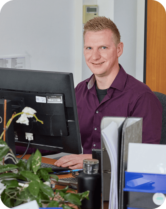 Teamleiter Kundenservice Freundlicher Mann mit auberginfarbenem Hemd sitzt am Computer und arbeitet